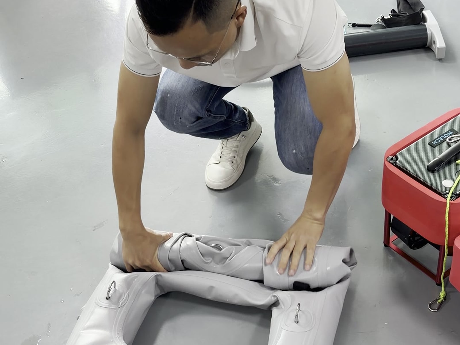 An inflatable platform being folded on a grey floor with an equipment box alongside